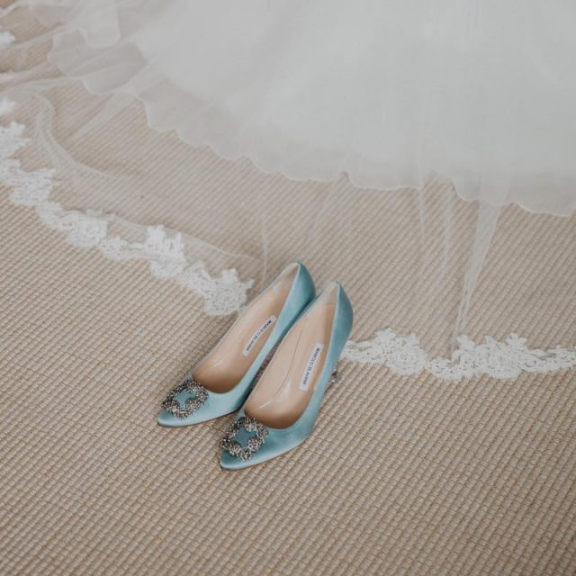 Close up photo of blue wedding shoes with the bride's wedding dress in the background. This wedding in Cornwall was planned by Jenny Wren - wedding planner.