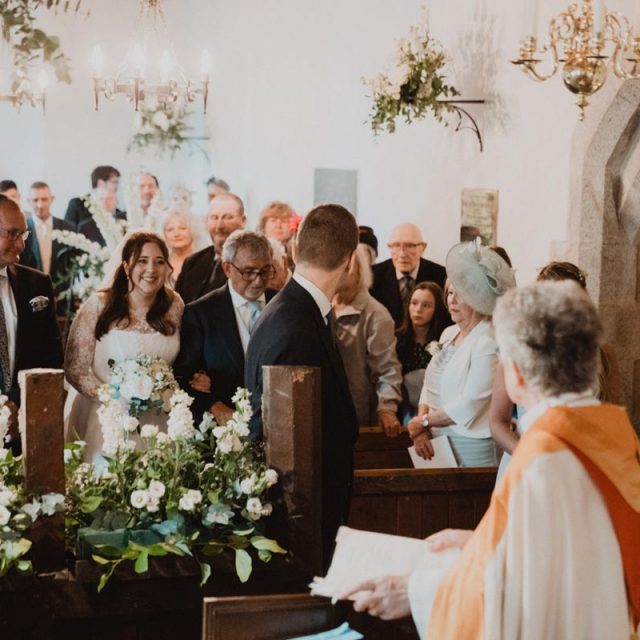 Bride walking down the aisle with her father as the groom looks back to see her. This wedding in Cornwall was planned by Jenny Wren - wedding planner.