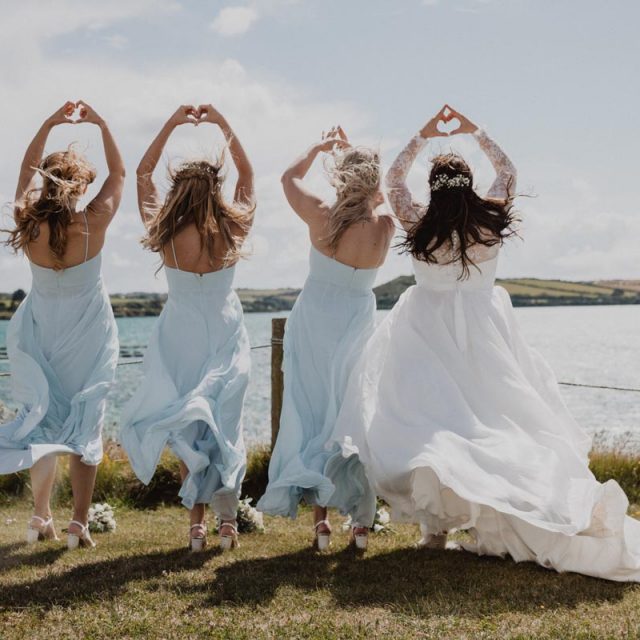 Bride with her bridesmaids jumping and celebrating by a lake. This wedding in Cornwall was planned by Jenny Wren - wedding planner.