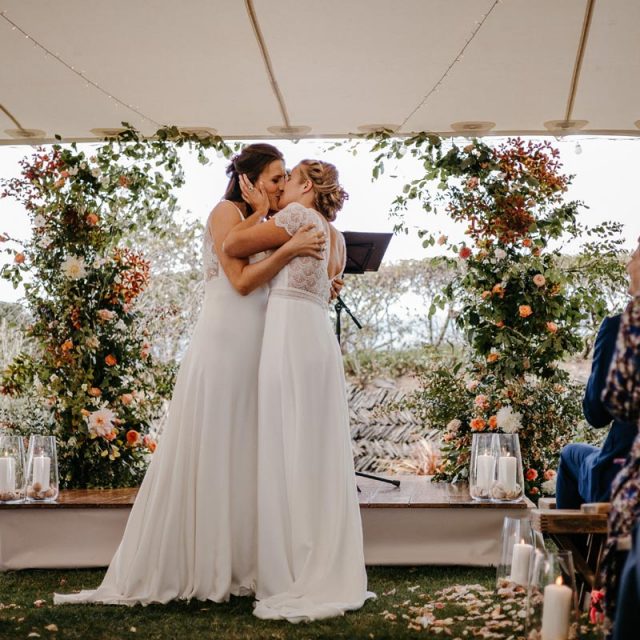 The happy couple embracing with a kiss for the first time in front of floral decorations.