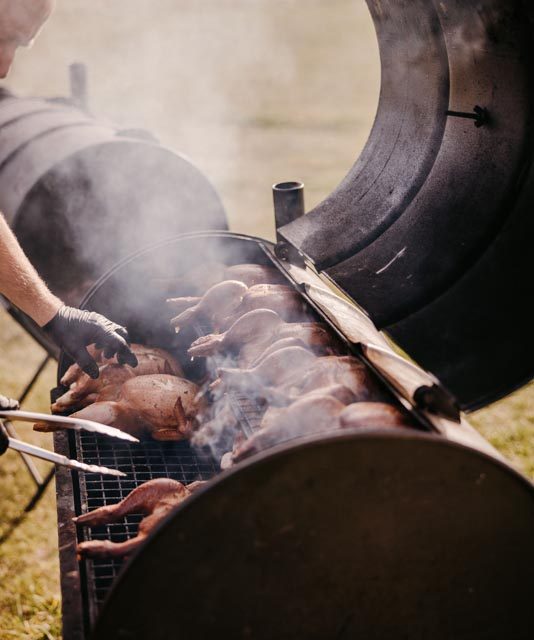 Man cooking several chickens on a barbecue at a wedding in Cornwall. This wedding was planned by Jenny Wren wedding planner.